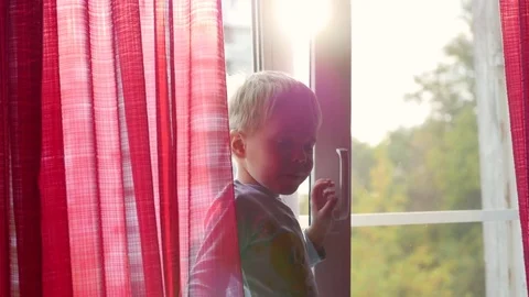 A child stands on the windowsill and looking out the window at the sun. on the Vidéo 80047799