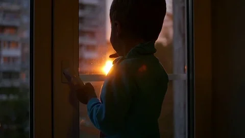 A child stands on the windowsill and looking out the window at the sun. Sunset Video stock 80809468