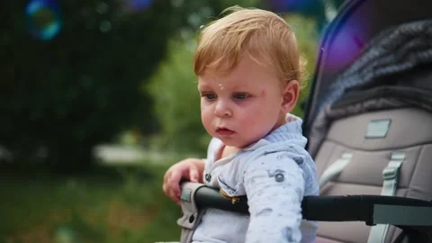 Child in stroller looks at bubbles floating in sunlight Stock Footage 340890113
