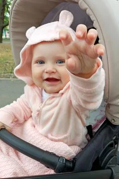 Child in stroller reaching out while sitting in a park on a sunny day Stock Photos