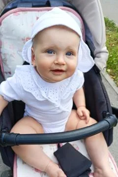 Child in a stroller smiles while sitting outdoors on a sunny day in a park Stock Photos