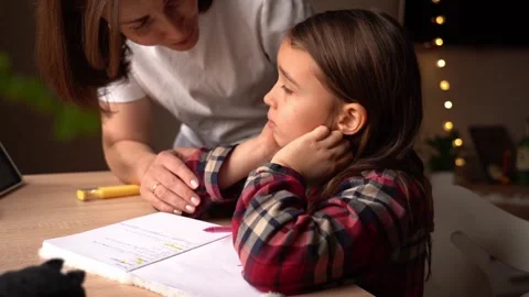 Child struggles with homework while mother offers support in cozy home Video stock 313484187