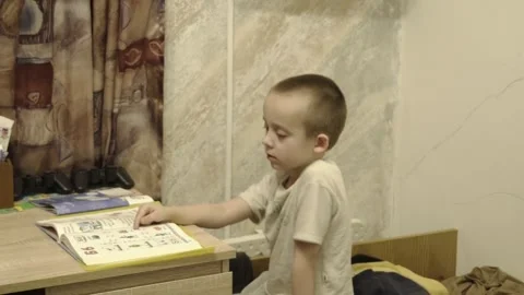 Child studies at a desk in a small room with books and papers on a table during Stock Footage 331244856