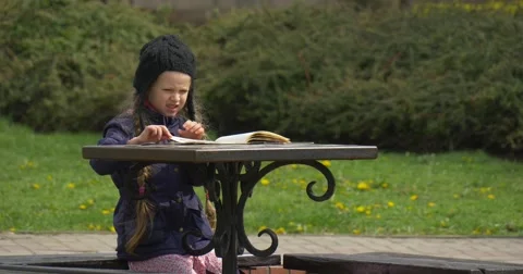 A Child in a Summer Cafe Looking Book. Stock Footage 62675431