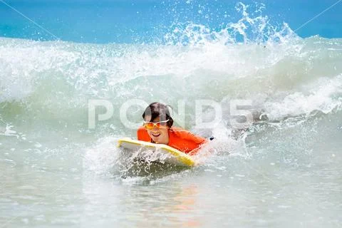 Child surfing on tropical beach. Surfer in ocean. Stock Photos