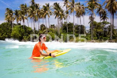 Child surfing on tropical beach. Surfer in ocean. Stock Photos