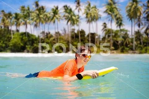 Child surfing on tropical beach. Surfer in ocean. Stock Photos