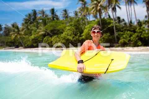 Child surfing on tropical beach. Surfer in ocean. Stock Photos