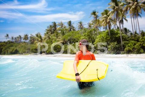 Child surfing on tropical beach. Surfer in ocean. Stock Photos