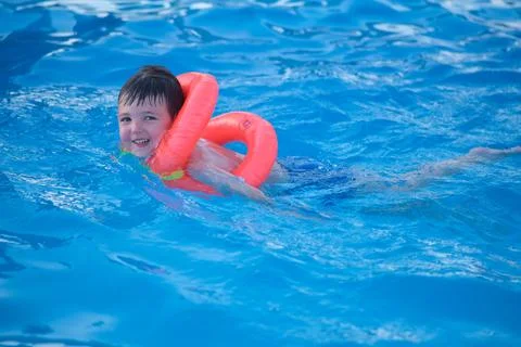 Child swimming in pool with orange floaty. Happy boy learning to swim in blue Stock Photos