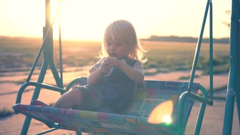 Child on a swing in the rays of the setting sun. Slow Motion. Stock Footage 95727575