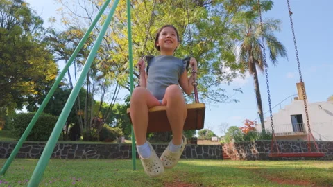 Child Swinging Joyfully Under Clear Blue Skies in a Park Stock Footage 335985328