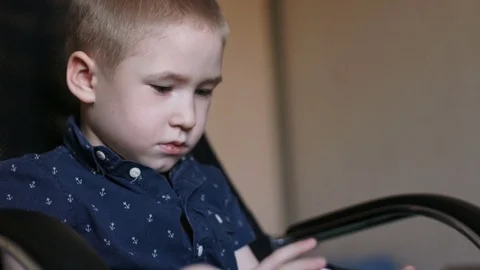 A child with a tablet, watching cartoons. Sits in an office chair Stock Footage 74978991
