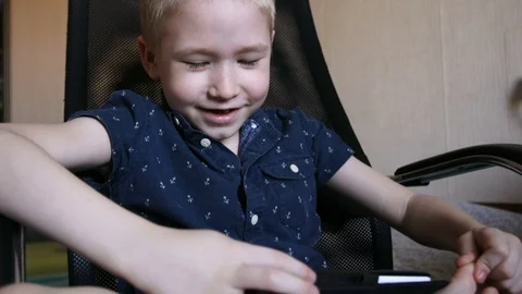 A child with a tablet, watching cartoons, smiling. Sits in an office chair Stock Footage 74978432