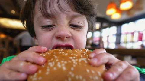 Child takes a bite of hamburger. Closeup face little kid holding burger eat.. Stock Footage 235980155