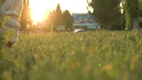 The child takes the first steps on the green grass, accompanied by his mother Stock Footage 143285185