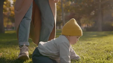 Child takes first steps in the park while mother supports him Stock Footage 303545759