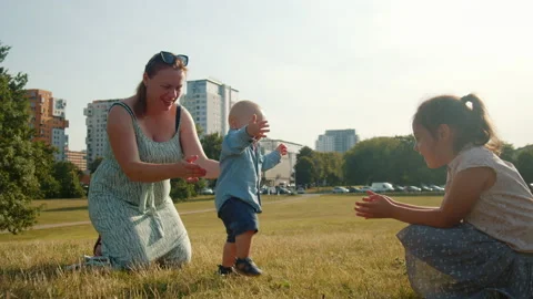 Child takes the first steps walking in the park with mom. Video stock 205616010