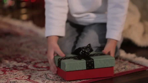 Child takes a gift - a box with a bow near the Christmas tree Stock Footage 145366331