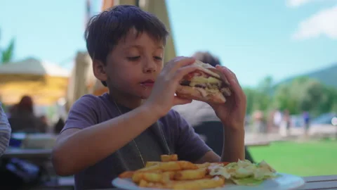 Child taking big bite of cheeseburger during outdoor cafe meal capturing en.. Stock Footage 342827845