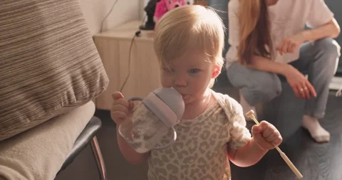 Child taking first unsupported steps indoors while holding everyday items Stock Footage 338995514
