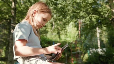 Child taps screen on digital tablet during outdoor homeschooling session under Stock Footage 346723971