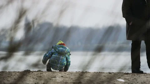 Child Throwing Sand into a River. Man Walking Nearby Stock Footage 80290603