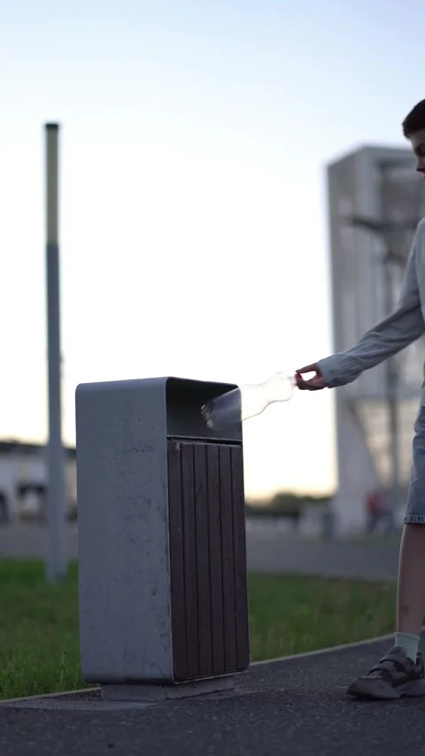 Child throws empty bottle into public garbage can on sidewalk Stock Footage 341895017