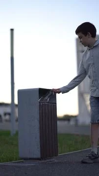 Child throws empty bottle into public garbage can on sidewalk, highlighting.. Stock Photos