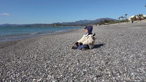 Child throws up a stone and tries to catch it sitting on the beach Stock Footage 124694586
