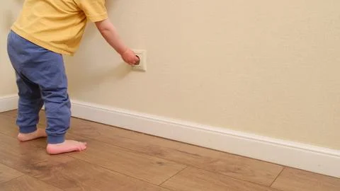Child touching electrical wall outlet with finger. Dangerous home situation a Stock Photos
