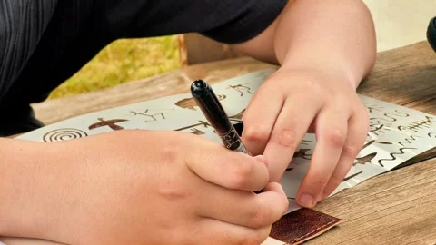 Child Tracing Tribal Patterns with Black Marker on Stencil Sheet Stock Footage 339044662