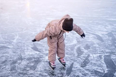 A child tries to keep balance while learning to skate on the ice rink of a fr Stock Photos