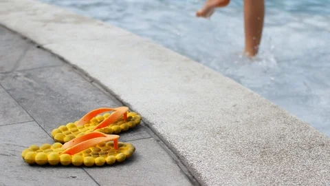 Child is trying water in the pool. Flip flops by the pool and feet in the water Stock Footage 123316375