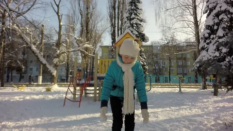 A child in a turquoise jacket blows snow from his hands. Stock Footage 87543279