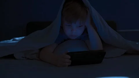 Child under blanket staring at smartphone at night Stock Footage 318603181