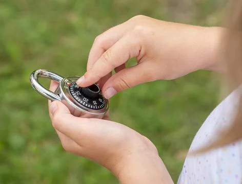Child unlocking a simple closed coded lock, holding a code padlock in hands.. Stock Photos