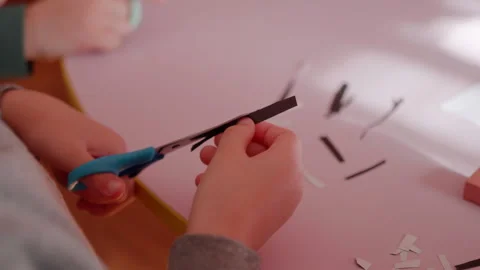 Child uses blue scissors to cut black and white paper strips on a pink table Stock-Footage 332893602