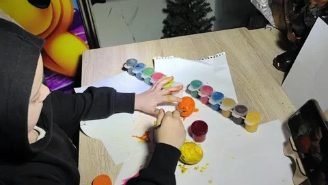 Child uses colorful paint to create art at a table in a home setting during even Stock Footage 328441318