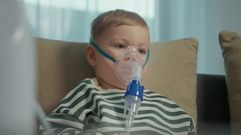 Child uses nebulizer mask for steam inhalation treatment at home Stock-Footage 346706659