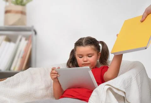 A child uses a tablet and refuses a book Stock Photos