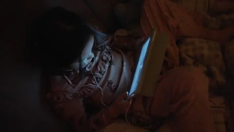 A child uses a tablet in dim light, showing engagement and playfulness before Video stock 303488051
