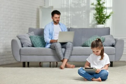 Child uses a tablet while caucasian father works from home Stock Photos