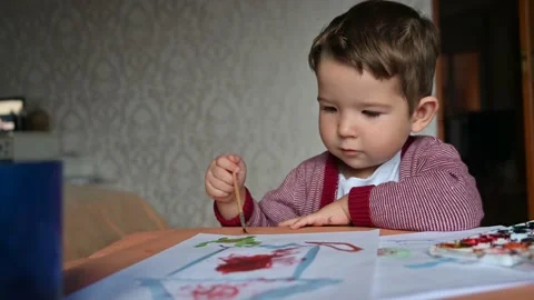 Child using brush and painting something on the paper. Cute drawing brunet child Stock Footage 186908386
