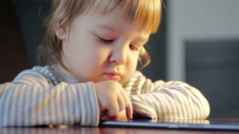 The child using digital device. Toddler is sitting at desk in lamplight, tapping Stock Footage 151703570