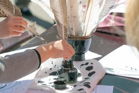 Child using feather quill and ink jar for writing on paper outdoors Stock Photos