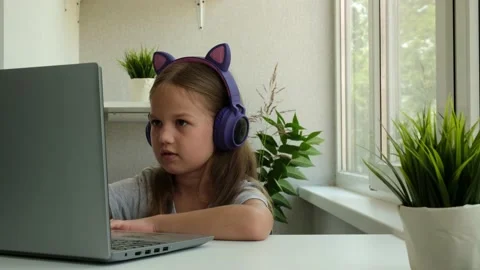 Child is using a laptop and study online at home. Little girl wears headphones Stock Footage 159632538
