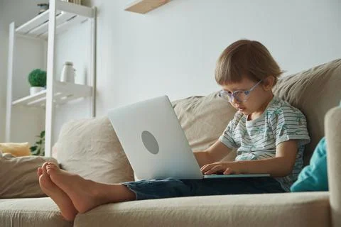 Child using laptop, sitting on sofa at home, Home schooling, distance learning Stock Photos