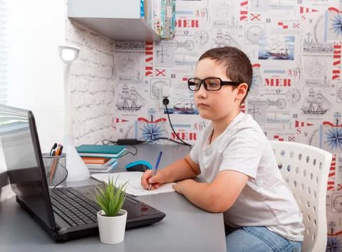 Child using laptop while sitting at desk with book and doing homework Foto stock