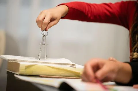 A child is using a metal drawing compass to measure or draw on a book. They a Stock Photos